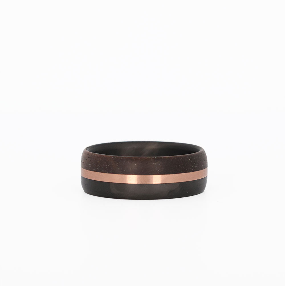 walnut wood and 14 karat rose gold wedding ring with carbon fiber sleeve laying flat